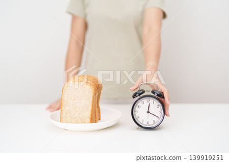 Happy smiling woman with whole wheat bread and alarm clock. concept of intermittent fasting, IF, meal timing, and choosing healthy carbohydrates for a balanced diet and weight loss management Happy smiling woman with whole wheat bread and alarm clock. concept of intermittent fasting, IF, meal timing, and choosing healthy carbohydrates for a balanced diet and weight loss management 139919251