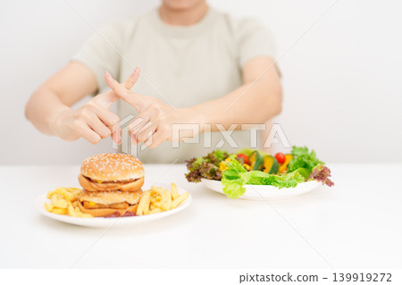 woman showing Rejecting and refusing with Hamburger. Healthy and Unhealthy Food Choice, Calories and Nutrition of vegetables Salad and Hamburger. dieting, weight loss, junk food and lifestyle woman showing Rejecting and refusing with Hamburger. Healthy and Unhealthy Food Choice, Calories and Nutrition of vegetables Salad and Hamburger. dieting, weight loss, junk food and lifestyle 139919272