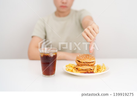 woman showing thumbs down, Rejecting and refusing with Juicy beef burger, potato chips and carbonated Soft drinks. Unhealthy, High calorie, Fast food craving, Obesity, diet, weight loss and junk food 139919275