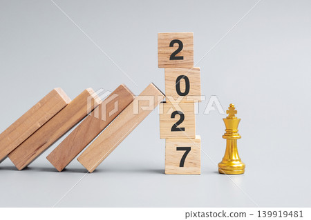 wooden Dominoes falling against 2027 stop blocks with golden Chess King figure. Business, Risk Management, Solution, economic, Insurance and New Year concept wooden Dominoes falling against 2027 stop blocks with golden Chess King figure. Business, Risk Management, Solution, economic, Insurance and New Year concept 139919481