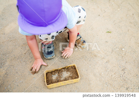 A close-up of a toddler's hands engrossed in playing in the sand, and a scene of outdoor play. 139919548