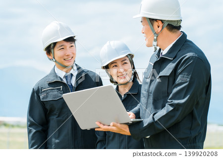 建築工地上,身著工作服的男女工人一邊開會,一邊看著筆記型電腦 建築工地上,身著工作服的男女工人一邊開會,一邊看著筆記型電腦 139920208