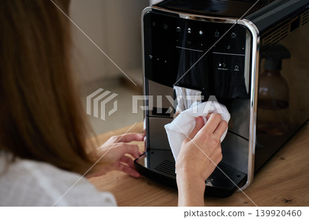 Person cleaning automatic coffee machine with cloth in kitchen 139920460