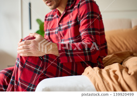 Man suffering from knee pain while massaging leg on bed 139920499