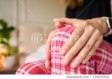Person suffering from knee pain while massaging knee on bed Person suffering from knee pain while massaging knee on bed 139920504