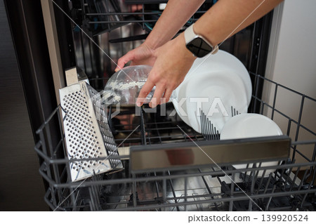 Hands loading dirty glass bowl into open dishwasher rack 139920524