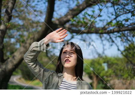 A woman shields herself from the summer sun with her hands. A woman shields herself from the summer sun with her hands. 139921022