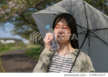 在強烈的陽光下，一名女子撐著陽傘，用塑膠瓶降溫臉部。 139921037