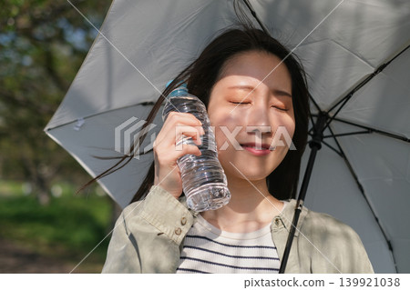 在強烈的陽光下,一名女子撐著陽傘,用塑膠瓶降溫臉部。 在強烈的陽光下,一名女子撐著陽傘,用塑膠瓶降溫臉部。 139921038