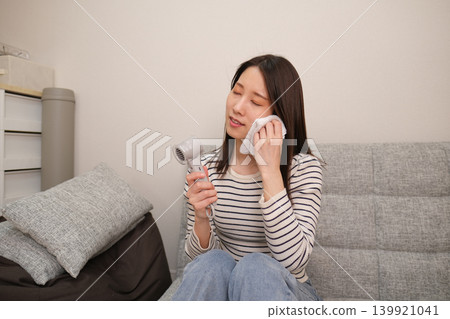A woman using a handheld fan to cool herself inside her home. A woman using a handheld fan to cool herself inside her home. 139921041