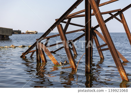 A weathered rusty metal structure extends into blue sea A weathered rusty metal structure extends into blue sea 139921068