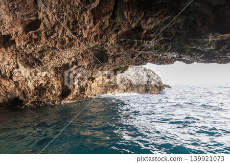 Sea cave frames a view of tranquil blue waters and an open sky Sea cave frames a view of tranquil blue waters and an open sky 139921073