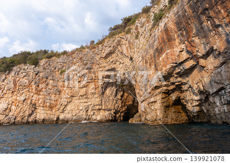 Red rocky cliffs rise above the sea water, showcasing weathered stone formations 139921078