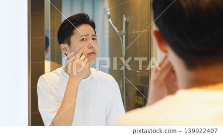 一位中年男子對著鏡子檢查自己的皮膚。 一位中年男子對著鏡子檢查自己的皮膚。 139922407
