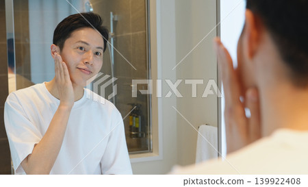 一位中年男子對著鏡子檢查自己的皮膚。 一位中年男子對著鏡子檢查自己的皮膚。 139922408