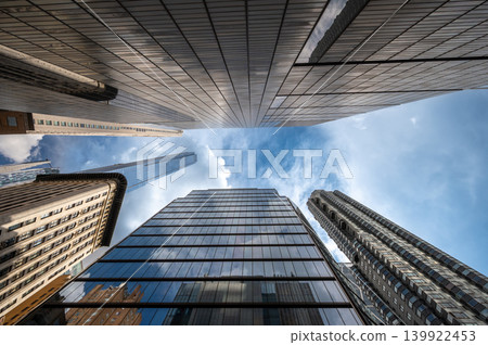 New york, usa august 20,2024. Urban architecture from below with modern buildings reflecting the blue sky and clouds, creating a sense of height and perspective in manhattan New york, usa august 20,2024. Urban architecture from below with modern buildings reflecting the blue sky and clouds, creating a sense of height and perspective in manhattan 139922453