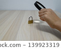 A hand examining a key with a magnifying glass 139923319