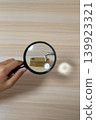 A hand examining the unlocked lock with a magnifying glass. 139923321