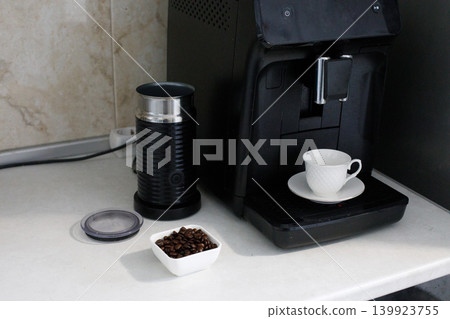 In a kitchen, a coffee machine is on the countertop. Coffee beans are next to the machine. In a kitchen, a coffee machine is on the countertop. Coffee beans are next to the machine. 139923755