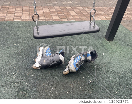 Skates left on the ground near a swing in a playground during a cloudy day in the afternoon Skates left on the ground near a swing in a playground during a cloudy day in the afternoon 139923771
