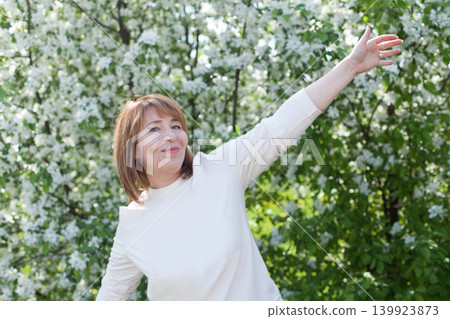 Excited mid adult woman in park on fresh spring flowers and green leaves background Excited mid adult woman in park on fresh spring flowers and green leaves background 139923873