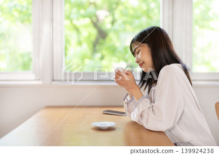 一位年輕的日本女子在靠窗的桌旁享用咖啡。 139924238