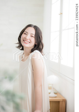 一位女士在自然光充足的房間裡微笑,展現出美麗和自然的生活方式;她直視鏡頭。 一位女士在自然光充足的房間裡微笑,展現出美麗和自然的生活方式;她直視鏡頭。 139924424
