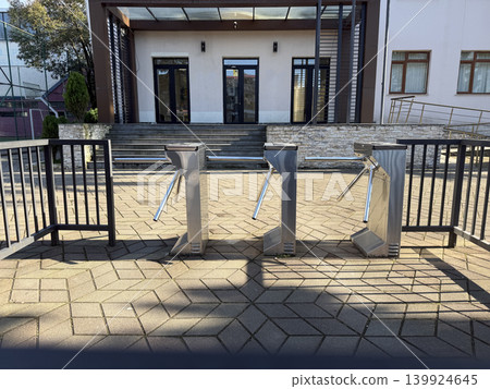 Turnstiles stand in front of a building with stairs and a fence at a public location during daytime Turnstiles stand in front of a building with stairs and a fence at a public location during daytime 139924645