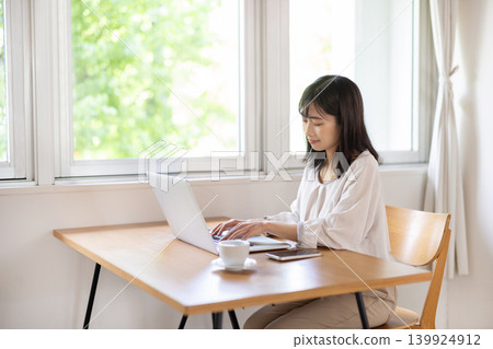 A young Japanese woman working on her laptop at a bright window table. A young Japanese woman working on her laptop at a bright window table. 139924912