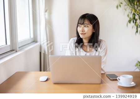 A young Japanese woman working on her laptop at a bright window table. A young Japanese woman working on her laptop at a bright window table. 139924919