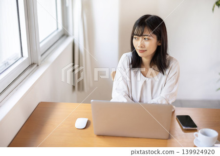 A young Japanese woman working on her laptop at a bright window table. A young Japanese woman working on her laptop at a bright window table. 139924920