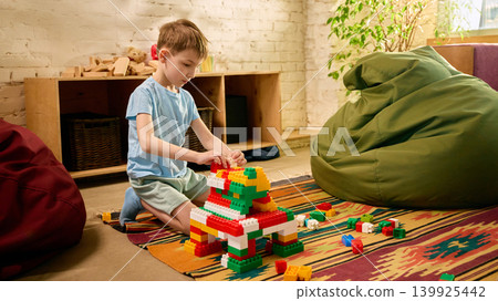 Boy building colorful block structure on rug in cozy sunny playroom. 139925442