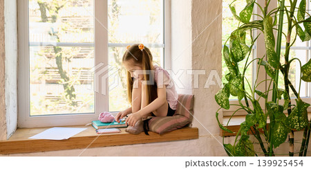Girl sitting on windowsill with craft materials and green plants. Girl sitting on windowsill with craft materials and green plants. 139925454