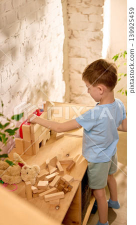 Boy building wooden block castle in warm creative playroom corner. Boy building wooden block castle in warm creative playroom corner. 139925459