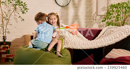 Laughing children playing with toy net on beanbag in sunny room. Laughing children playing with toy net on beanbag in sunny room. 139925460