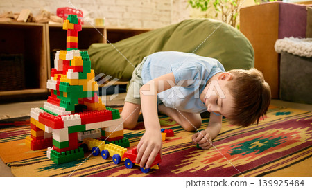 Boy playing with toy vehicle near colorful block house in cozy playroom. Boy playing with toy vehicle near colorful block house in cozy playroom. 139925484