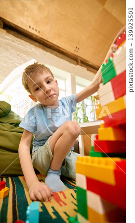 Smiling boy building colorful block tower on playroom rug. Smiling boy building colorful block tower on playroom rug. 139925501