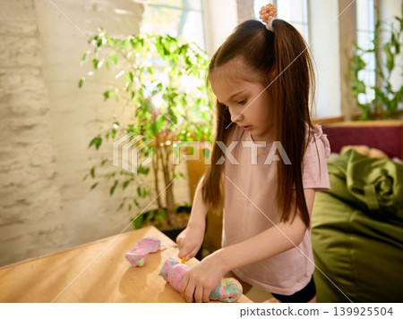 Focused girl shaping colorful modeling clay in sunny creative playroom Focused girl shaping colorful modeling clay in sunny creative playroom 139925504