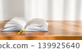 Open book on a wooden table with soft morning light from left 139925640