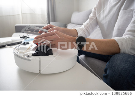 Man cleaning and maintaining robotic vacuum cleaner at home Man cleaning and maintaining robotic vacuum cleaner at home 139925696