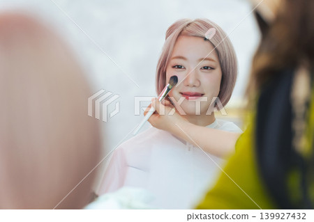A woman with light-colored hair getting her hair and makeup done. A woman with light-colored hair getting her hair and makeup done. 139927432