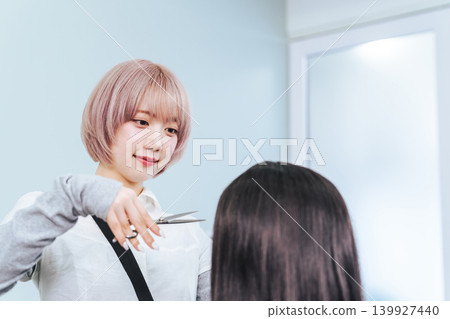 A female staff member with light-colored hair cutting hair. A female staff member with light-colored hair cutting hair. 139927440