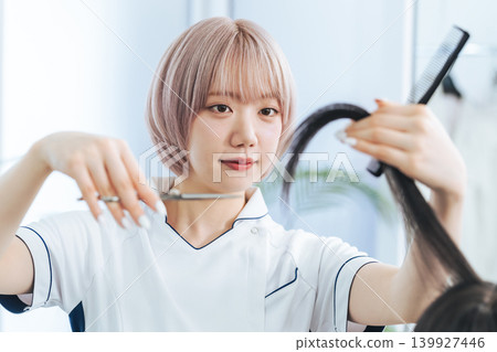 A female staff member with light-colored hair cutting hair. A female staff member with light-colored hair cutting hair. 139927446