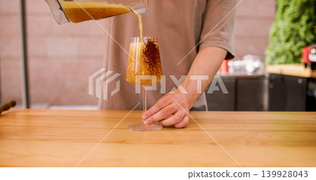 Cocktail pouring. Beverage serving. Unrecognizable chef man hand preparing drink from jar in decorating glass liquid with cocoa powder coating in cafeteria. 139928043