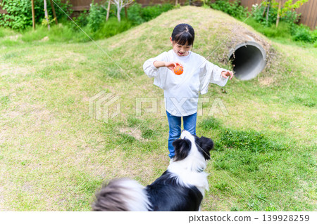 A girl and a dog playing outdoors. 139928259