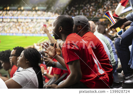 Focused football supporters watching dramatic final minutes of live soccer match from crowded stadium stands with red scarves. Sports fans asking for the final whistle in the stadium. Focused football supporters watching dramatic final minutes of live soccer match from crowded stadium stands with red scarves. Sports fans asking for the final whistle in the stadium. 139928724