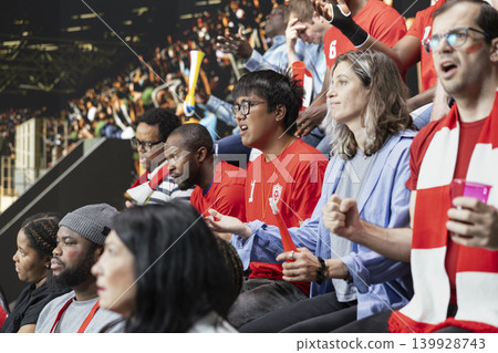 Diverse football supporters watching a tense last minute play during live soccer match in stadium stands with passionate crowd reactions. Passionate fans react to close call with anticipation. Diverse football supporters watching a tense last minute play during live soccer match in stadium stands with passionate crowd reactions. Passionate fans react to close call with anticipation. 139928743