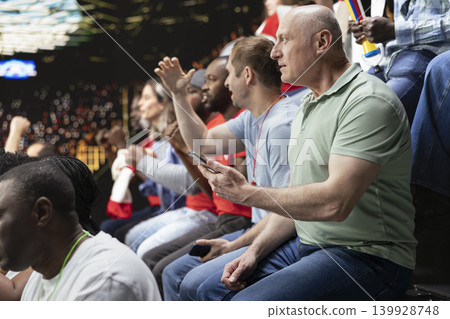 Stadium supporter checking online betting apps and live odds on phone, watching dramatic football match with diverse crowd of cheering fans. Enthusiast follow high risk live betting, bet ticket. Stadium supporter checking online betting apps and live odds on phone, watching dramatic football match with diverse crowd of cheering fans. Enthusiast follow high risk live betting, bet ticket. 139928748