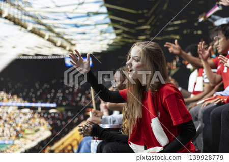 Young woman football supporter gesturing with open hands in frustration during tense soccer game, red scarf and stadium crowd behind. Inclusive football community, heartbreak and disbelief. Young woman football supporter gesturing with open hands in frustration during tense soccer game, red scarf and stadium crowd behind. Inclusive football community, heartbreak and disbelief. 139928779
