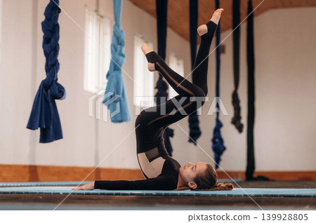 Legs are up, lying down. Child practicing yoga on a mat in a fitness studio Legs are up, lying down. Child practicing yoga on a mat in a fitness studio 139928805